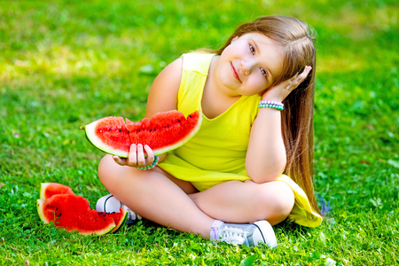 happy little girl eating watermelon outdoor in the summer parkの写真素材