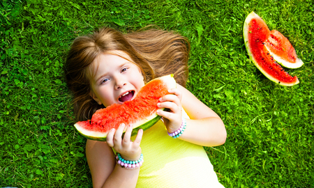 happy little girl eating watermelon outdoor in the summer parkの写真素材