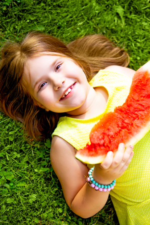 happy little girl eating watermelon outdoor in the summer parkの写真素材