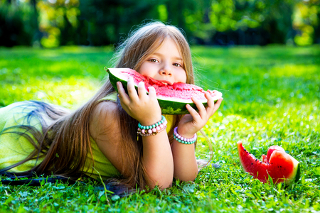 happy little girl eating watermelon outdoor in the summer parkの写真素材