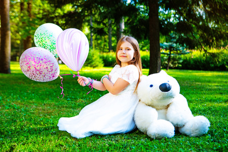 happy little girl  with many balloons and a teddy bear outdoor in the  summer parkの写真素材