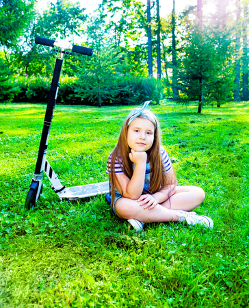 happy little girl riding a scooter outdoor in the  summer parkの写真素材
