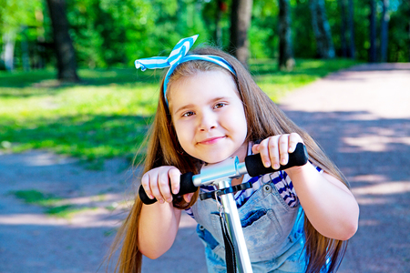 happy little girl riding a scooter outdoor in the  summer parkの写真素材