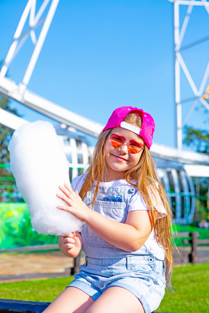 happy little girl eating cotton candy outdoor in the amusement summer parkの写真素材