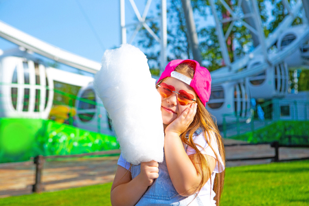happy little girl eating cotton candy outdoor in the amusement summer parkの写真素材