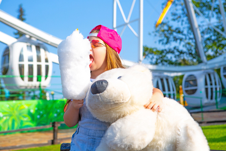 happy little girl eating cotton candy outdoor in the amusement summer parkの写真素材