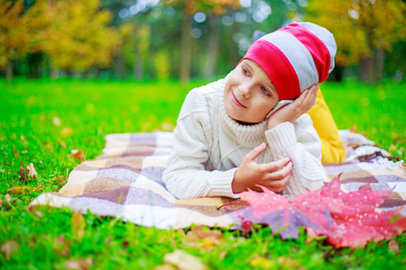 happy cute  boy talking on the phone in the autumn park with green grass and yellow leavesの写真素材