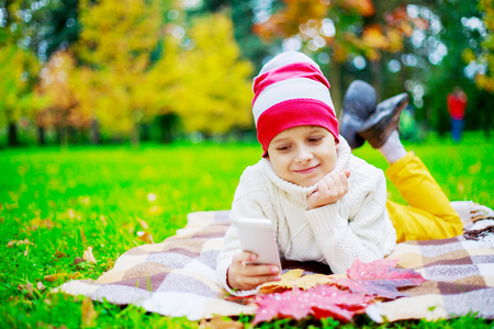 happy cute  boy in the autumn park with his cellphoneの写真素材
