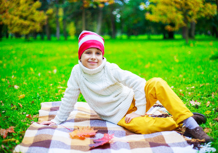 happy cute  boy in the autumn park with green grass and yellow leavesの写真素材