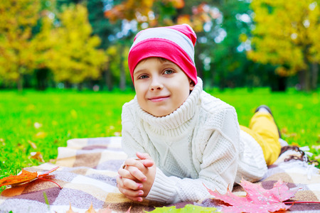 happy cute  boy in the autumn park with green grass and yellow leavesの写真素材