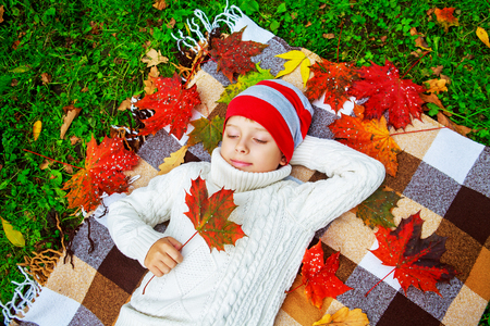 happy cute  boy in the autumn park with green grass and yellow leavesの写真素材