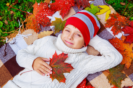 happy cute  boy in the autumn park with green grass and yellow leavesの写真素材
