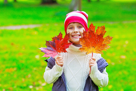 happy boy in the autumn park with yellow leaves in his handsの写真素材