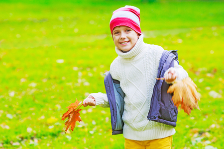 happy boy in the autumn park with yellow leaves in his handsの写真素材