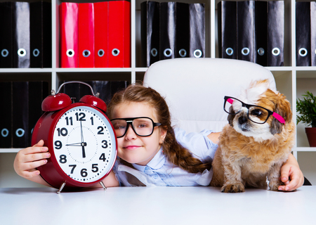 cute little girl wearing glasses with her dog and a clockの写真素材