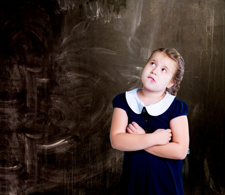 thoughtful  little girl   at school against chalkboardの写真素材