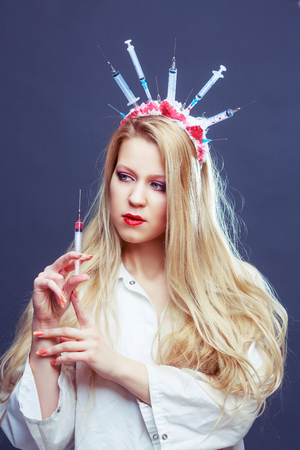 Halloween costume of a crazy nurse with crown made of syringes and a syringe in the handの写真素材