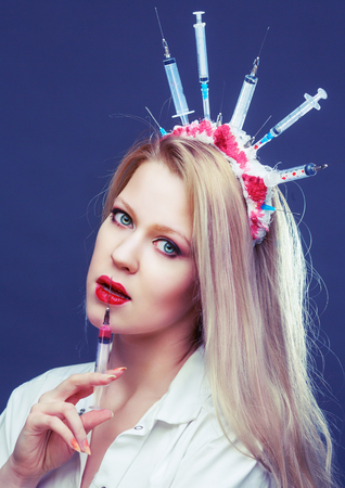 Halloween costume of a crazy nurse with crown made of syringes and a syringe in the handの写真素材