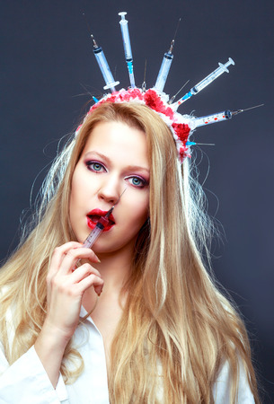 Halloween costume of a crazy nurse with crown made of syringes and a syringe in the handの写真素材