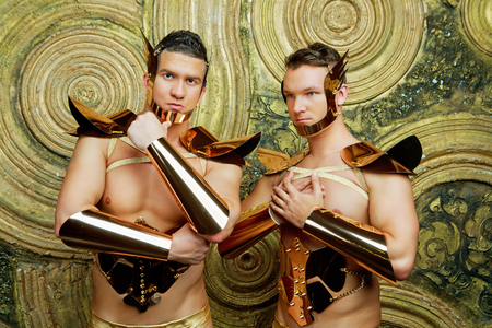 two striptease dancers wearing costumes with golden armour in the studio against golden studio backgroundの写真素材