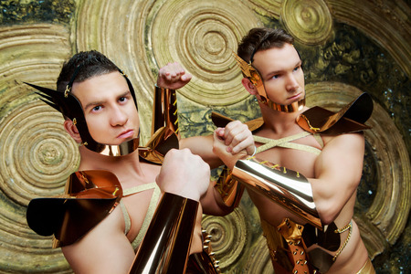 two striptease dancers wearing costumes with golden armour in the studio against golden studio backgroundの写真素材