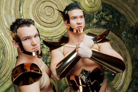 two striptease dancers wearing costumes with golden armour in the studio against golden studio backgroundの写真素材