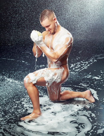 a handsome muscular attractive young man taking a shower with a sponge and shower gelの写真素材