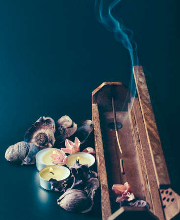 incense stick aroma with smoke in a wooden handmade holder with dried petals and candles isolated on backgroundの写真素材