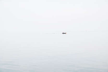 Seascape in the style of minimalism. Small fishing boat is minimal far in blue sea between sky and...