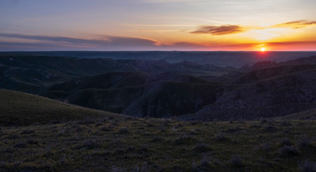 The sky turns warm colors as the sun sets behind the distant mountains, creating a stunning natural...