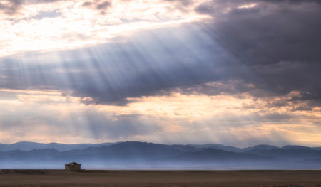small lonely clay house in the desert, steppe or prairie under a cloudy sky with rays of sunの写真素材