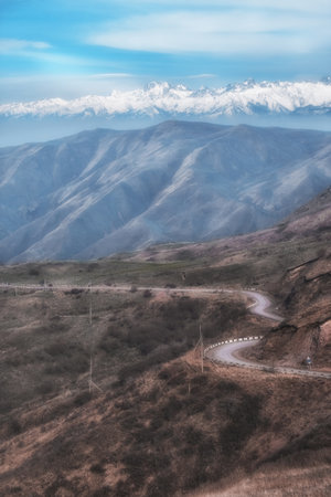 A winding road climbs the Ushkonyr mountain plateau, with Talgar Peak towering above, Almaty,...
