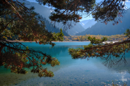 Issyk Lake in autumn. The crystal clear water reflects the sky and the mountains, and the golden trees on the shore create a picturesque frame for this mountain landscape.の写真素材