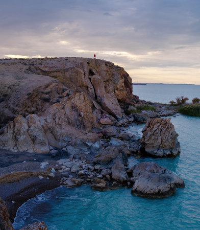 A lonely traveler on the edge of a rocky cliff, contemplating the endless turquoise waters of Lake...