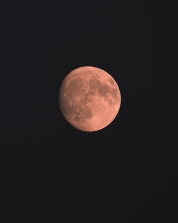 A close-up of the Moon in the waning or growing phase, illuminated by a warm orange-red light that highlights the details of the lunar seas and craters against the background of the deep night sky.の写真素材