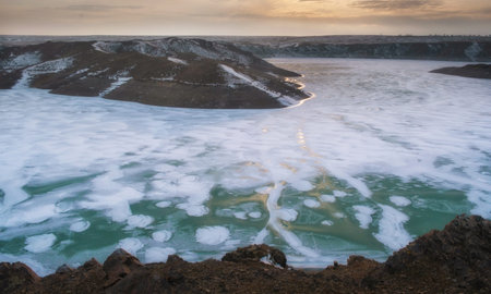 A fascinating view of the partially frozen Kurty reservoir in the Almaty region. Icy patterns on the water and dry shores contrast with the rugged hills in the background.の写真素材