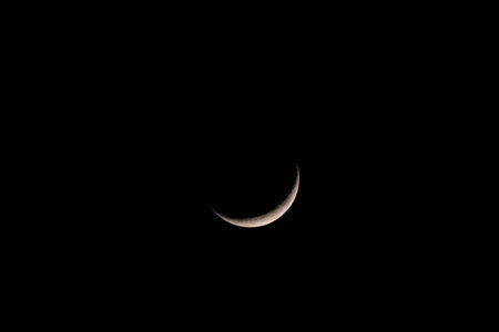 Thin crescent moon glowing in the pitch black night sky. Minimalist celestial background with vast...