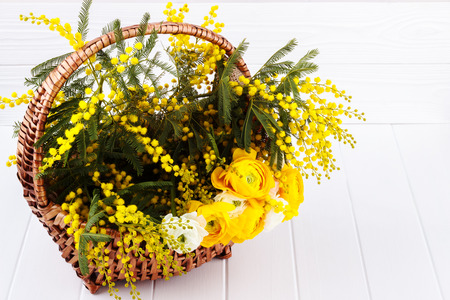 Mimosa and Ranunculus flowers in a basket on wooden table. Spring holidays backgroundの写真素材