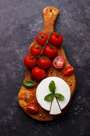 ricotta cheese with basil and tomatoes on olive wood cutting board over black slate backgroundの写真素材