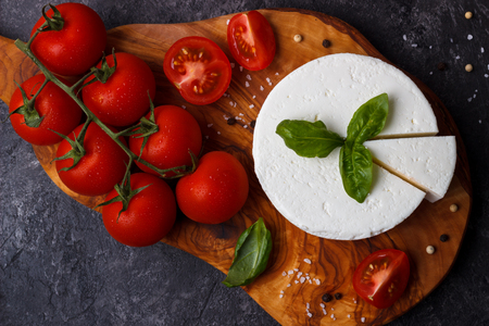 ricotta cheese with basil and tomatoes on olive wood cutting board over black slate backgroundの写真素材