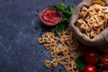 Whole grain raw italian pasta and ingredients composition on black rustic slate stone background, top view with copy spaceの写真素材