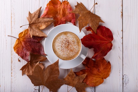 Hot coffee cappucino and autumn leaves on old white wooden background.Seasonal relax concept