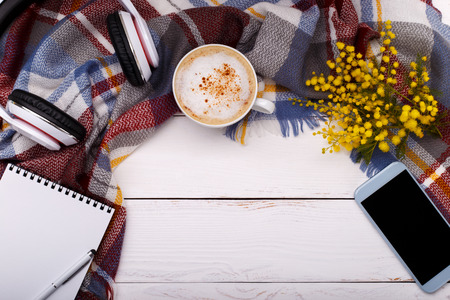 Hot coffee cappucino, blanket,mimosa flowers ,notepad,smartphone and head phones on old wooden background. Seasonal relax concept,flat layの写真素材