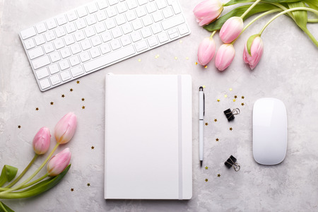 Workspace with keyboard, diary,pen,paper clips and pink tulips on gray stone background, flat lay.の写真素材