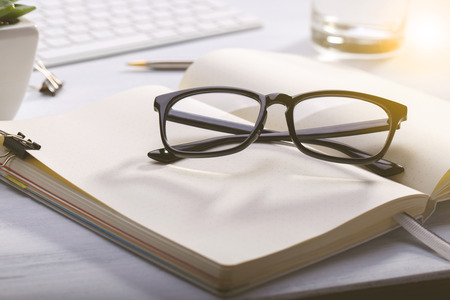 Open diary and glasses on modern desk, business or education concept, natural lightの写真素材