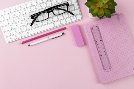 Workspace with keyboard, glasses, notepad, pen and succulent plant on pink background, flat lay.