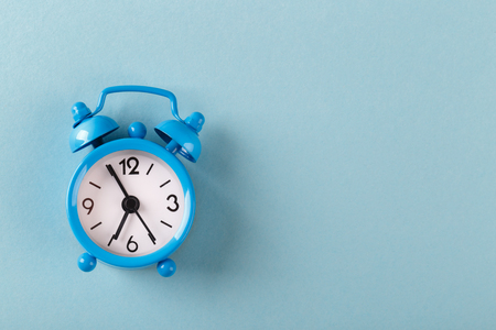 Small alarm clock on blue trendy background, flat lay copy space