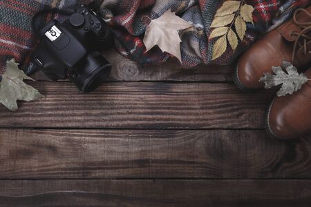 Traveler's or photographer's autumn concept, camera, boots and plaid on old barn wood background