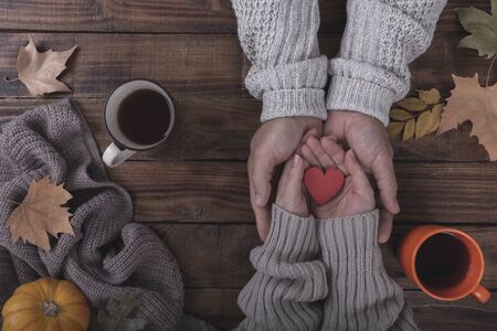 Couple in love drinking coffee and holding wooden heart in hands, autumn on the tableの写真素材