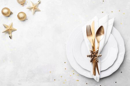 Christmas or new year table setting with golden cutlery and white napkin on white stone table, card...